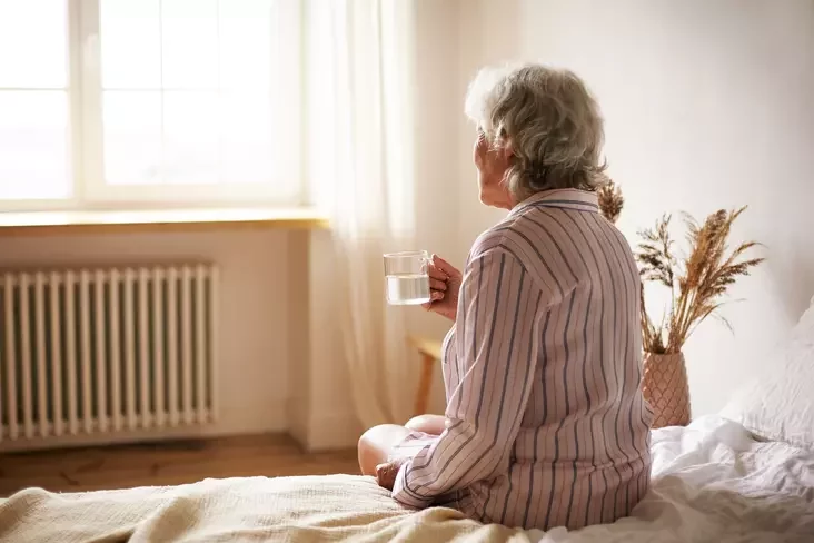 Old woman holding mug and sitting in the bedroom